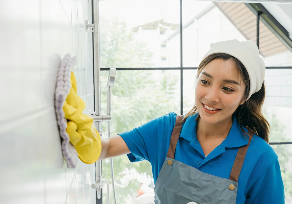 Professional house cleaner wiping bathroom shower wall